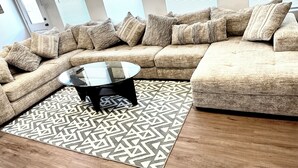 Un salon moderne avec un canapé d’angle, une table basse en verre et un tapis à motifs.
