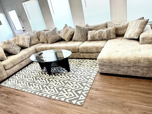 Ein modernes Wohnzimmer mit Ecksofa, Glastisch und einem gemusterten Teppich.