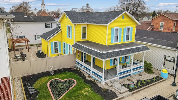 Una casa amarilla de dos pisos con un porche y un jardín en forma de corazón.