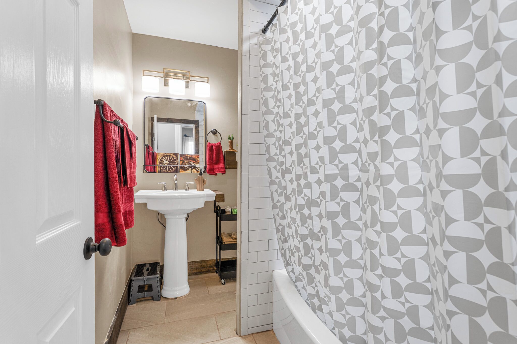 Une salle de bain avec un lavabo blanc, des serviettes rouges, un miroir et un rideau de douche à motifs géométriques.
