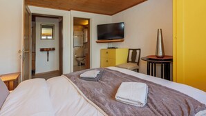 Et hotelværelse med seng, fjernsyn, et lille bord og et badeværelse, der kan ses gennem en åben dør.