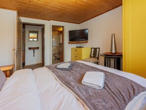 Habitació d'hotel amb un llit, una televisió, una taula petita i un bany visible a través d'una porta oberta.