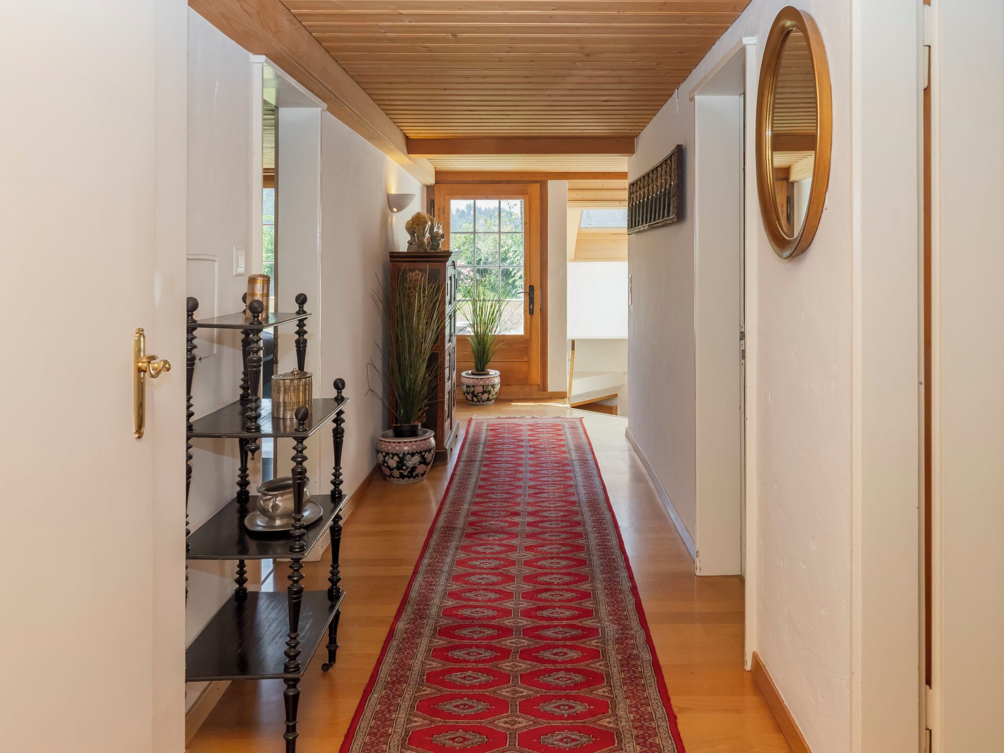 Un couloir avec un plafond en bois, une moquette rouge à motifs et un plancher en bois.