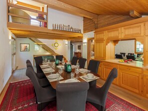 Un espace repas avec une longue table dressée pour six personnes, des meubles en bois et un escalier menant à un niveau supérieur.