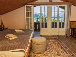 A bedroom with a large bed, a bench, a patterned rug, and a view of mountains through a sliding door.