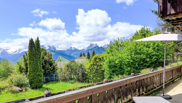 Balkon med udsigt til bjerge, et træhegn og et loungeområde med pude og parasol.