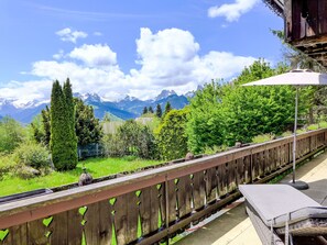 A balcony with a view of mountains, a wooden fence, and a lounge area with a cushion and umbrella.
