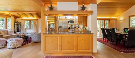 A spacious living area with a wooden ceiling, a kitchen with a central island, and a dining area with a red patterned rug.
