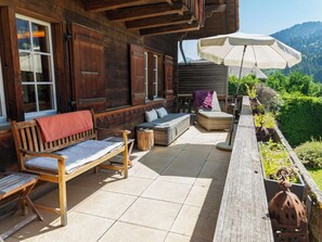 A wooden deck with a bench, a sofa, and a table, overlooking a mountainous landscape.