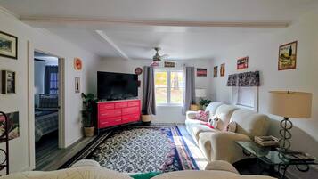 Ein Wohnzimmer mit Fernseher, rotem Schminktisch, weißem Sofa und einem gemusterten Teppich.
