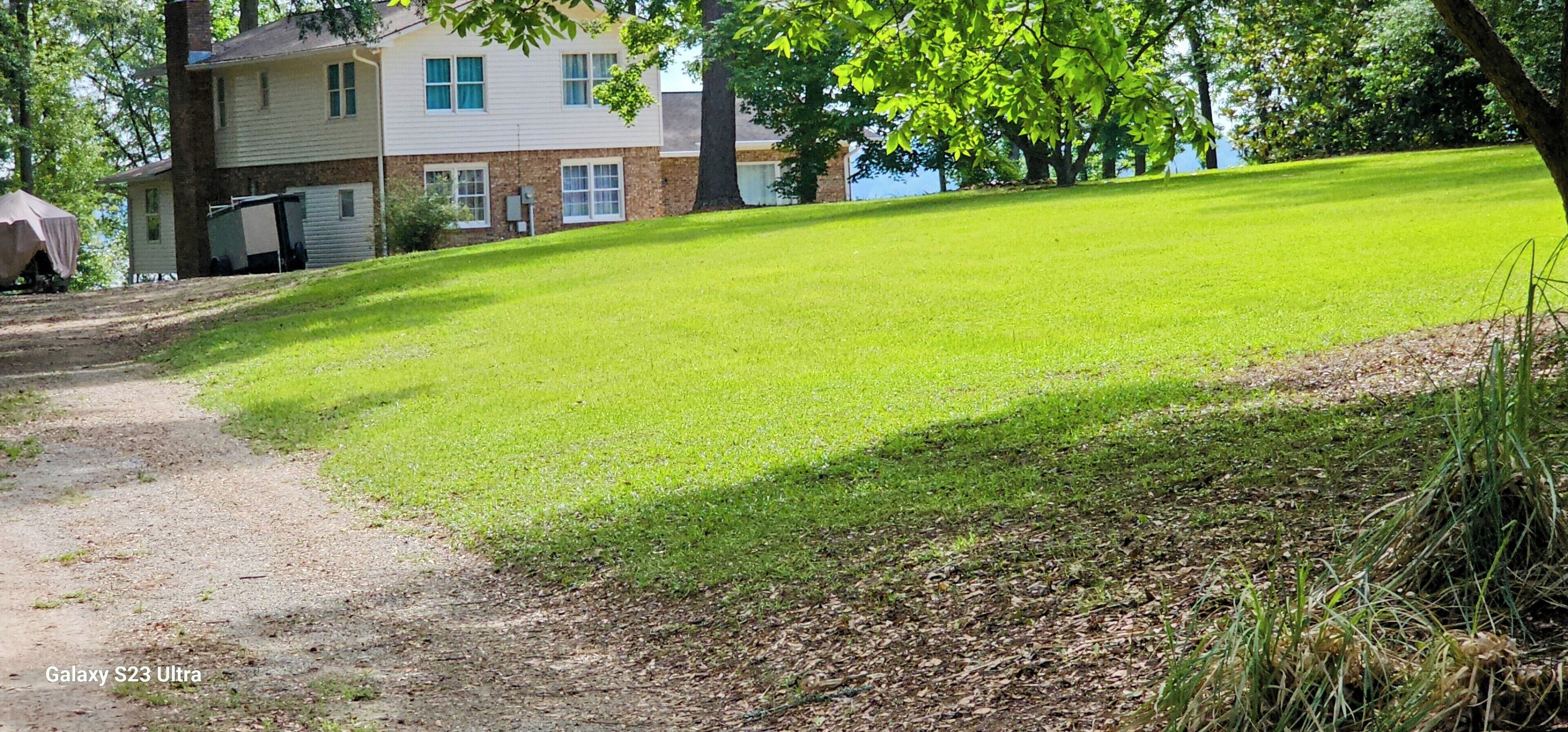 A residential area with a well-maintained lawn, a dirt path, and a house with a garage.