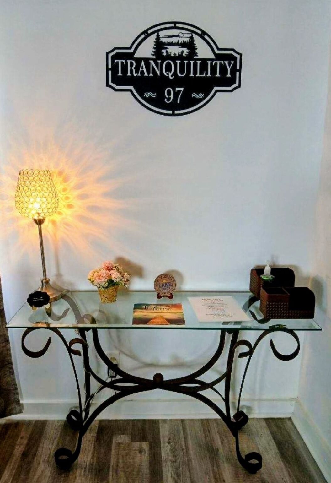 Un comptoir d’accueil avec une pancarte indiquant « TRANQUILLITÉ 97 », une lampe, une carte de bienvenue, un petit objet décoratif et une boîte de mouchoirs.