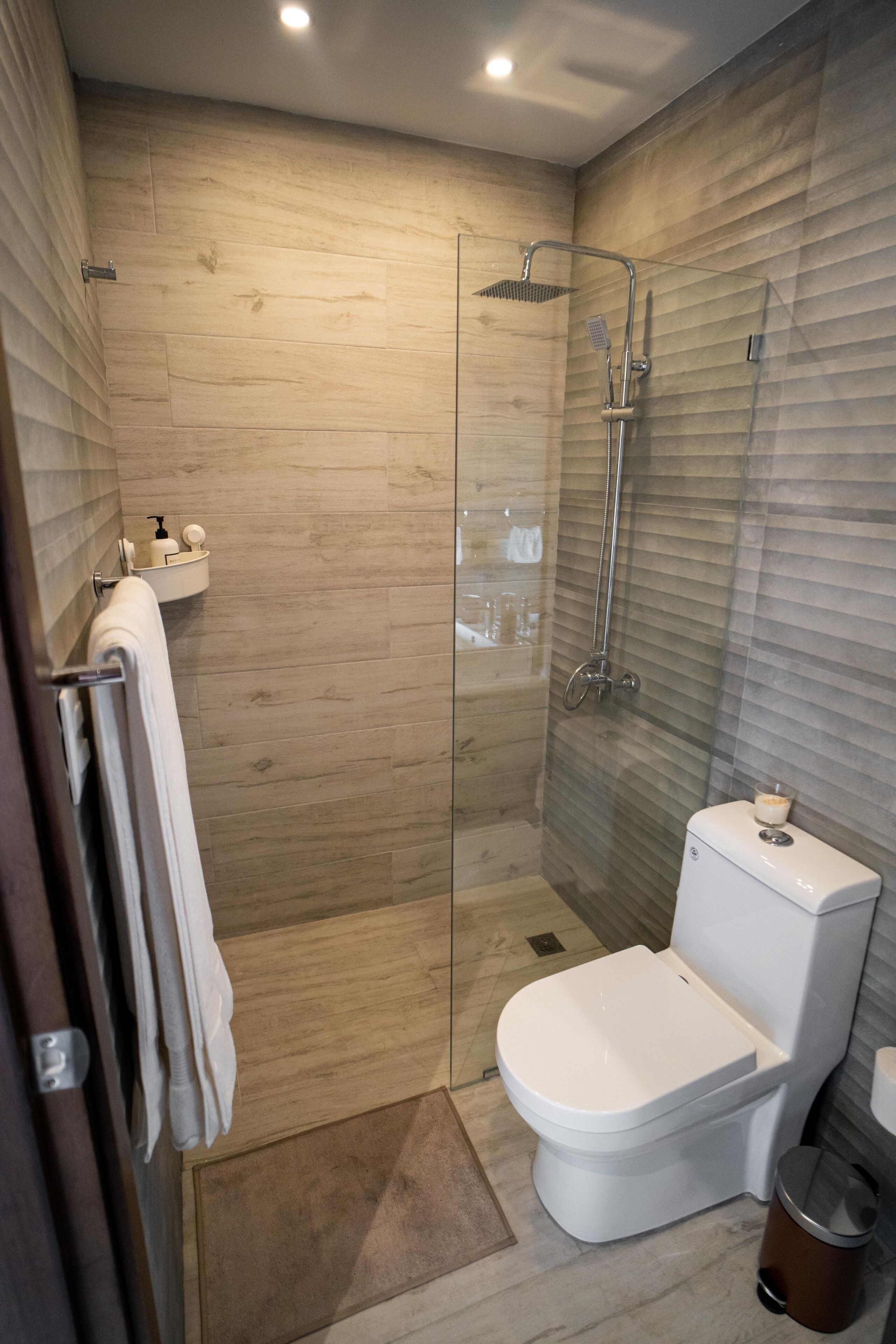 Une salle de bain moderne avec une douche à parois de verre, des toilettes blanches et une petite étagère contenant des articles de toilette.