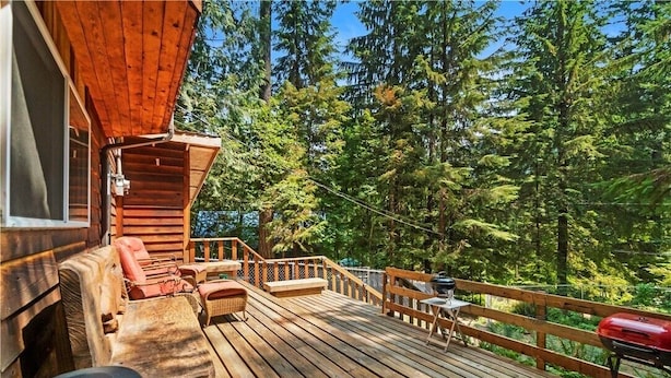 A wooden deck with outdoor furniture, a barbecue grill, and a view of a forested area. - Cedar-sided cabin, RV parking, Kids & Pet friendly (Ashford)