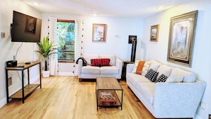 A living room with a sofa, a coffee table, a TV, and a plant. - Cedar-sided cabin, RV parking, Kids & Pet friendly (Ashford)
