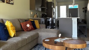 A modern living room with a sectional sofa, a round coffee table, and a kitchen in the background. - Haven at Greenbridge: Near SEA Airport & Downtown Seattle (Seattle)