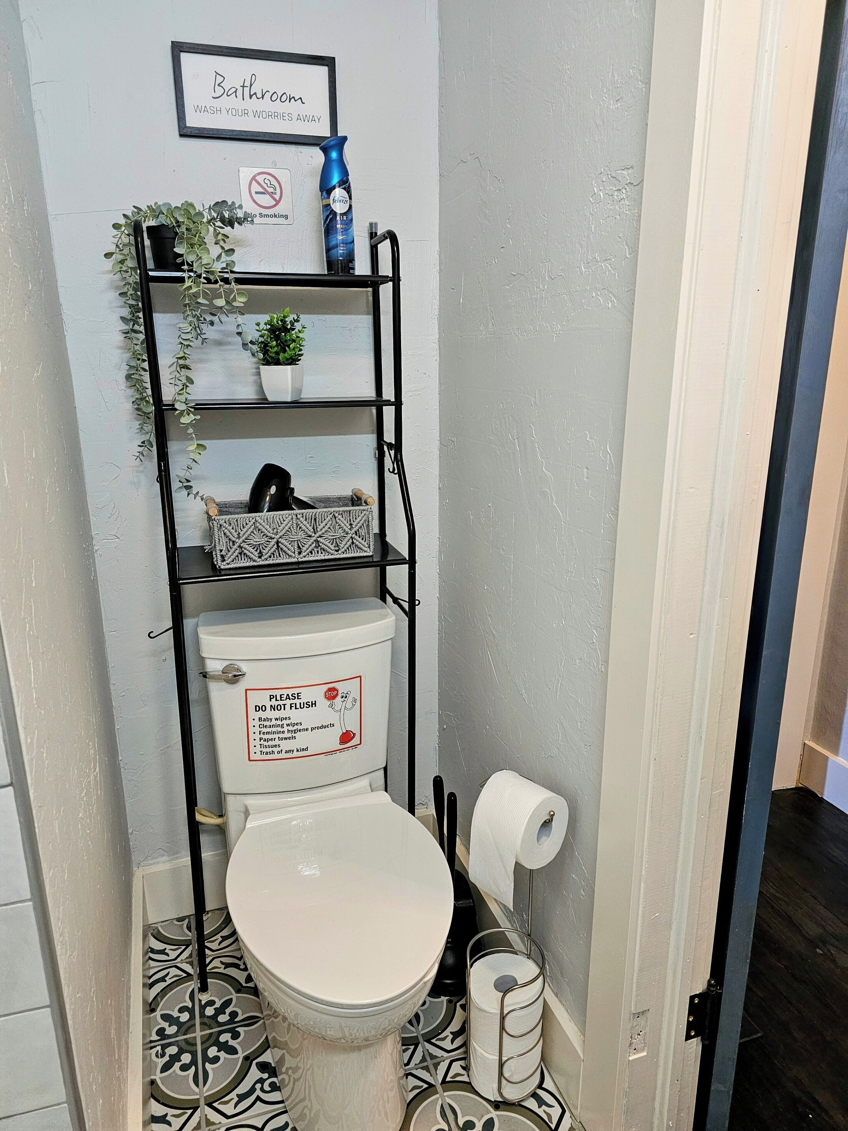 Un baño con inodoro, un estante con artículos de aseo, un cartel de 'No fumar' y un cartel que dice 'Por favor, tire la cadena'.