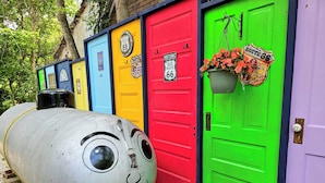 Colorful doors with Route 66 signs, a large metal object with a face, and a planter with flowers.