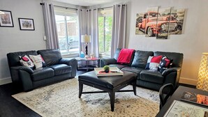 A modern living room with two black leather sofas, a coffee table, and a patterned rug.