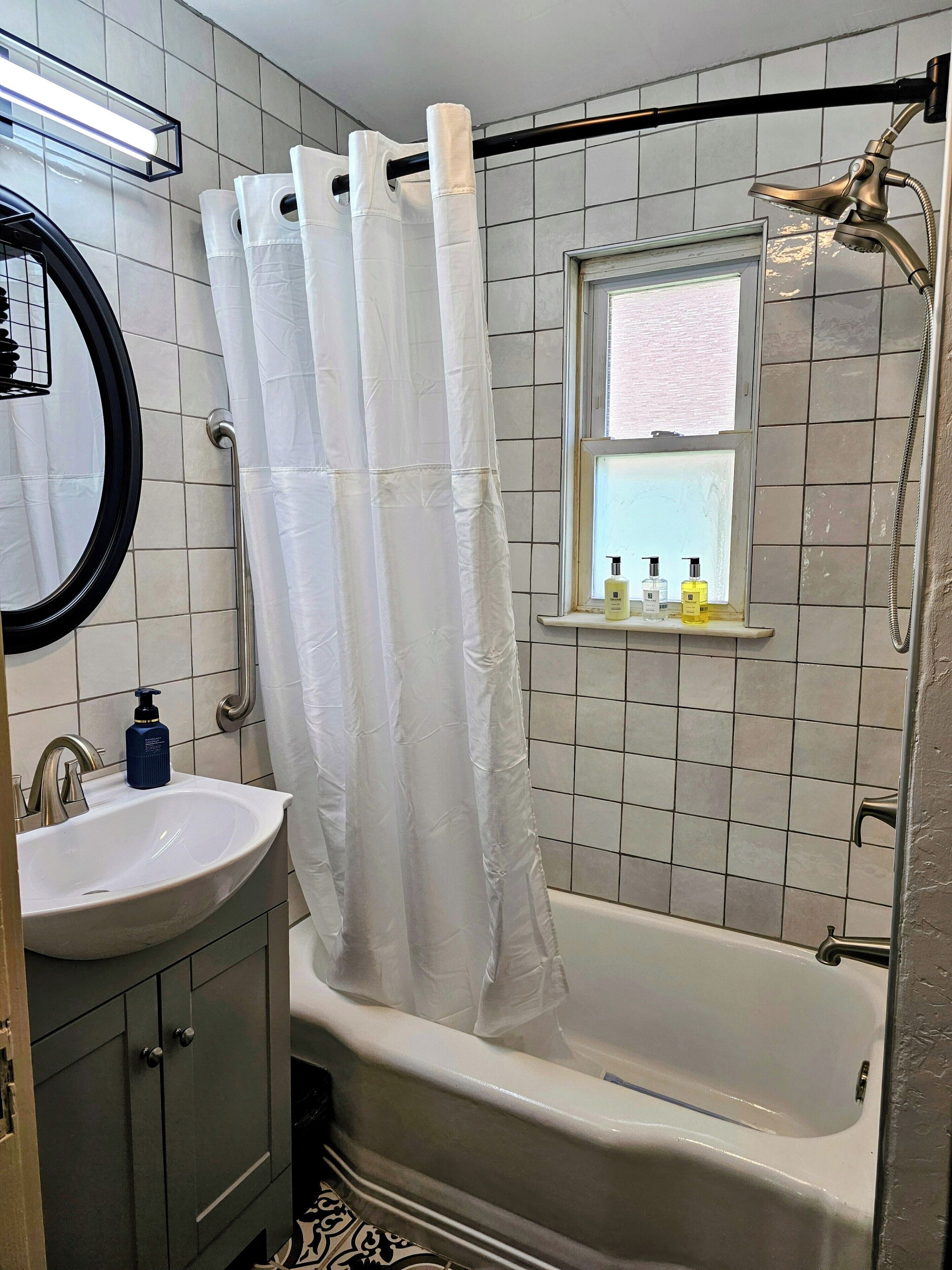 Une salle de bain avec une baignoire, une fenêtre, un lavabo et un miroir.