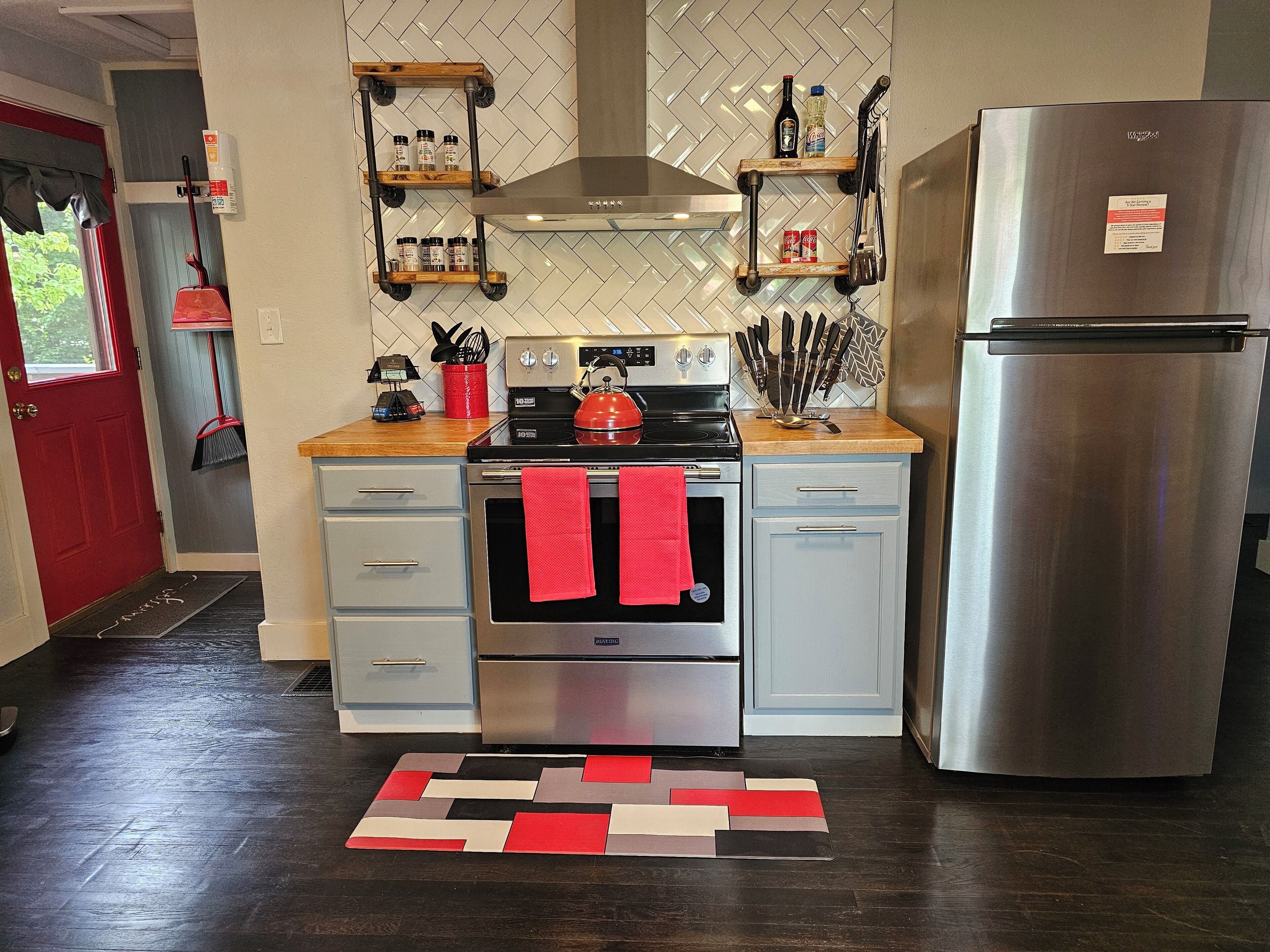 Een moderne keuken met roestvrijstalen apparatuur, houten planken en een vloerkleed met een rood-zwart patroon.