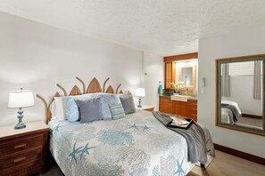 Un dormitorio con cama, mesitas de noche, un espejo y un baño visible a través de una puerta abierta.