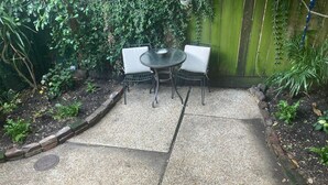 A patio area with a round table and two chairs, surrounded by a gravel path and a wooden fence. - Contemporary tiny home with loft bedroom in the Irish Channel, private courtyard (New orleans)