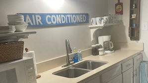A kitchen with a sink, a microwave, a dishwasher, and a coffee maker. There is a sign above the sink that says "AIR CONDITIONED". - Contemporary tiny home with loft bedroom in the Irish Channel, private courtyard (New orleans)
