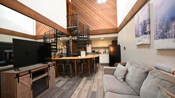 Ein modernes Interieur mit Holzboden, einer zentralen Wendeltreppe, einer Küchenzeile und einer Sitzecke mit einer Couch.