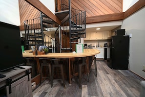 Une cuisine moderne avec un escalier en colimaçon, des tabourets de bar en bois et un téléviseur à écran plat.