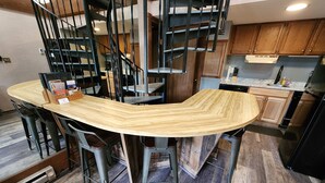 Eine Küche mit Kochinsel, Holzschränken und einer schwarzen Treppe.