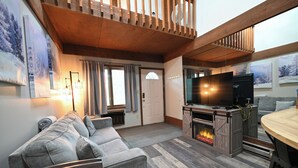 Ein gemütliches Wohnzimmer mit Kamin, einer Couch, einem Fernseher und einem Essbereich.