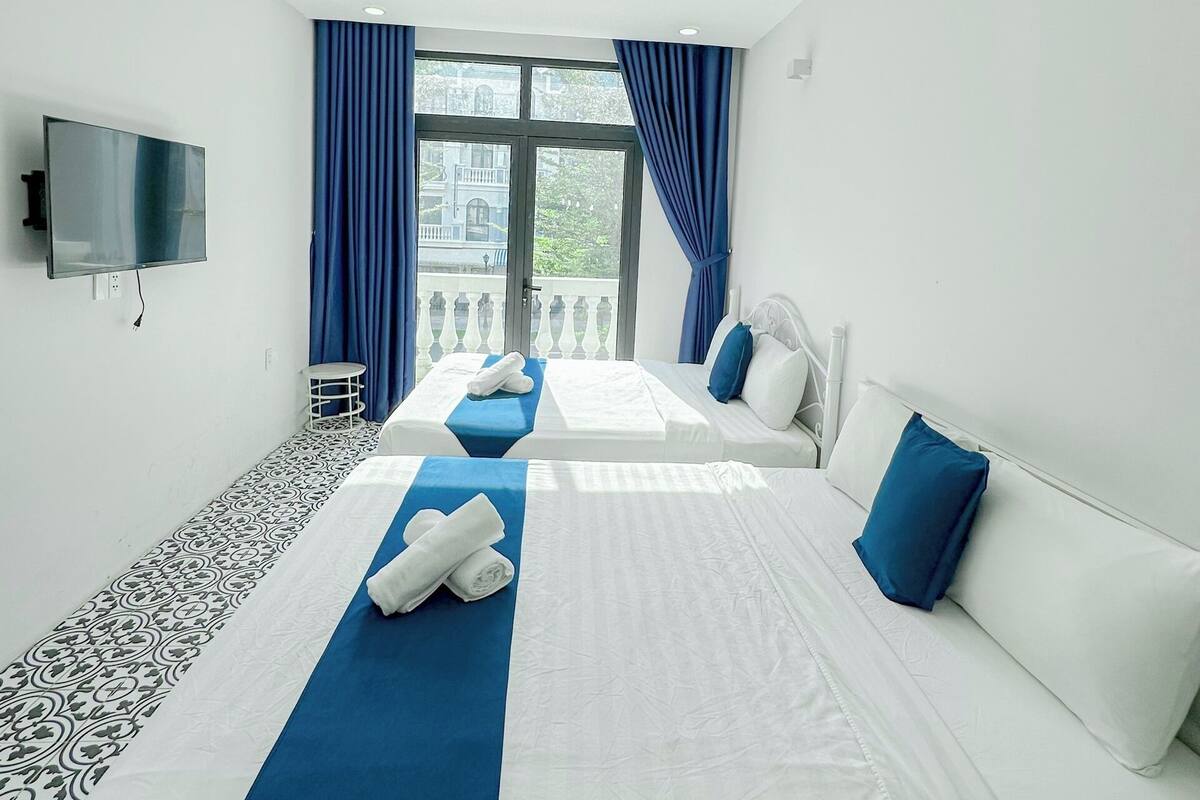 A hotel room with two beds, a TV, a small table, and a window with curtains.