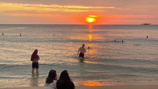A beach scene with people swimming and standing in the water during sunset. - Lala Boutique Phu Quoc (Phu Quoc)