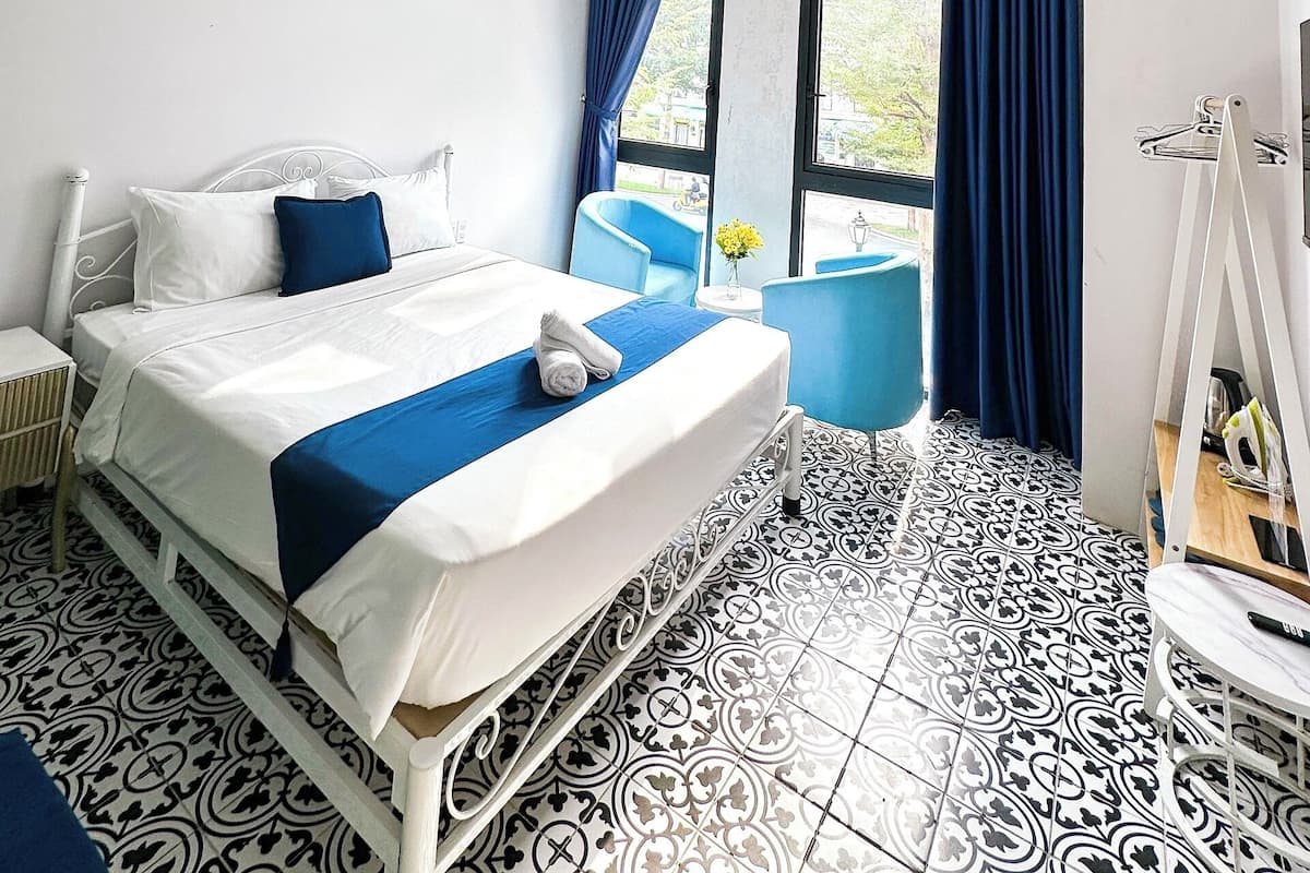 A hotel room with a bed, a chair, a small table, and a window with curtains.