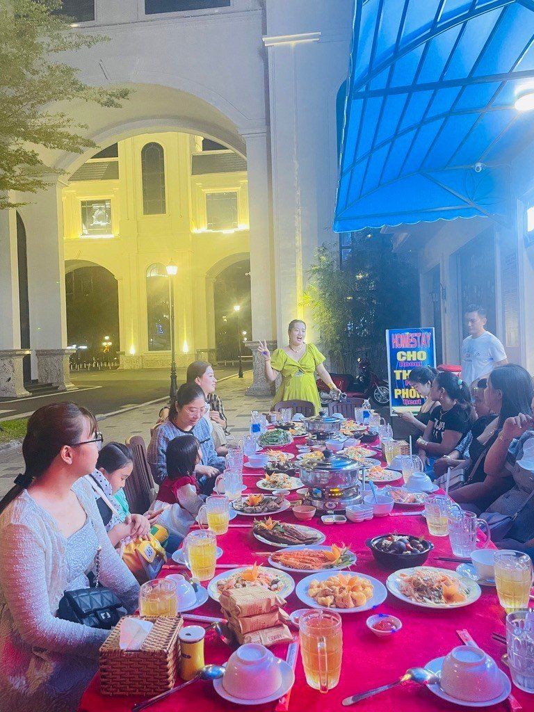 Un grupo de personas cenando en una mesa al aire libre, con diversos platos y bebidas.