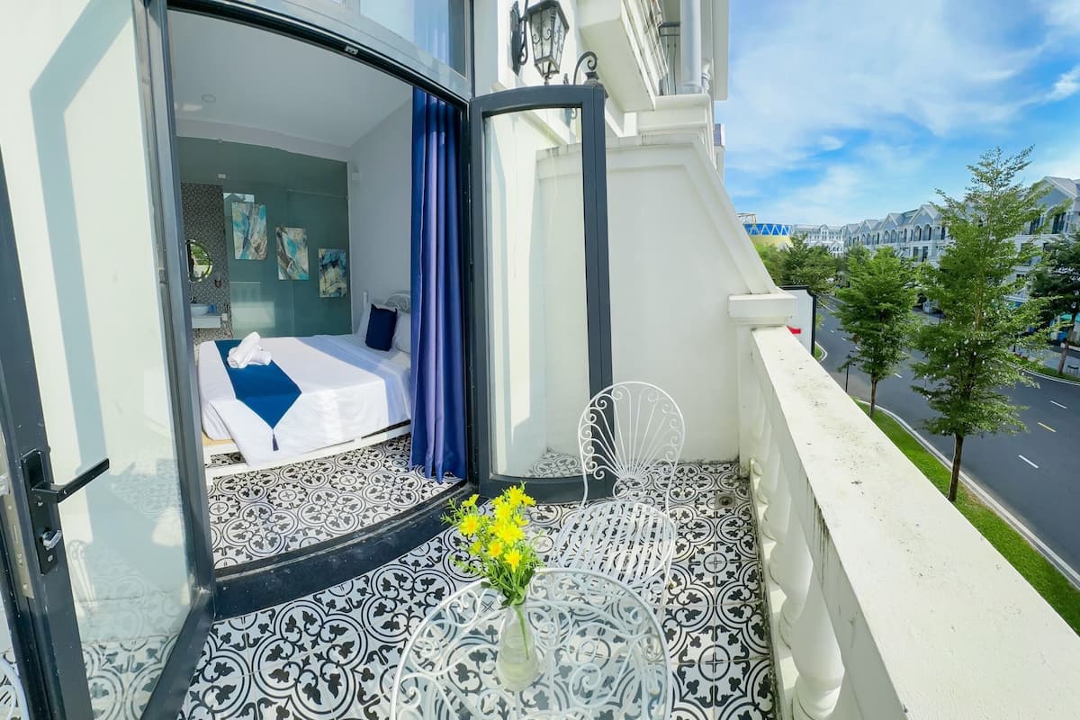 A hotel room with a bed, a bathroom, and a balcony with a view of the street.