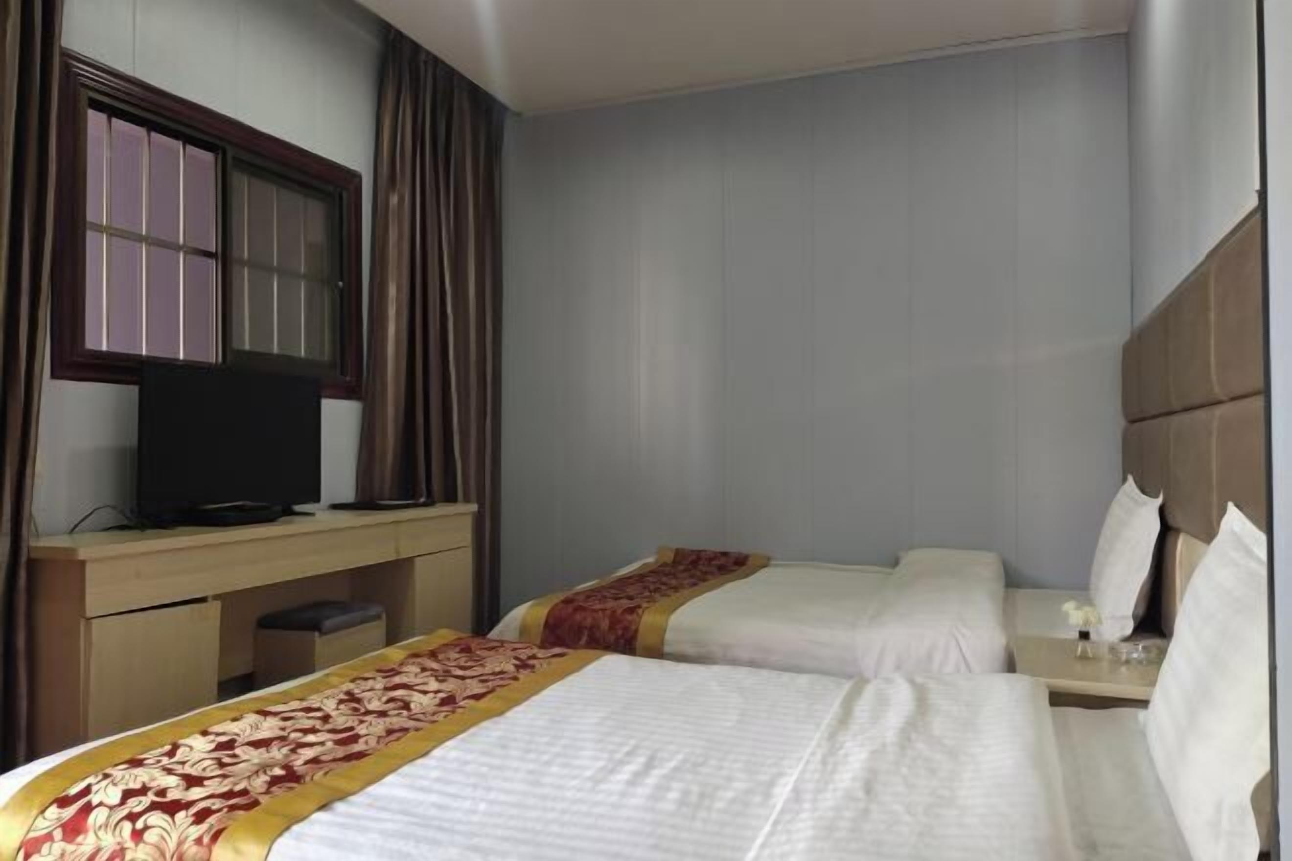 Habitación de hotel con dos camas, un televisor sobre un escritorio y una ventana con cortinas.
