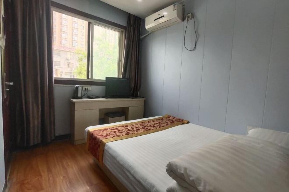 A bedroom with a bed, a desk, and an air conditioning unit.