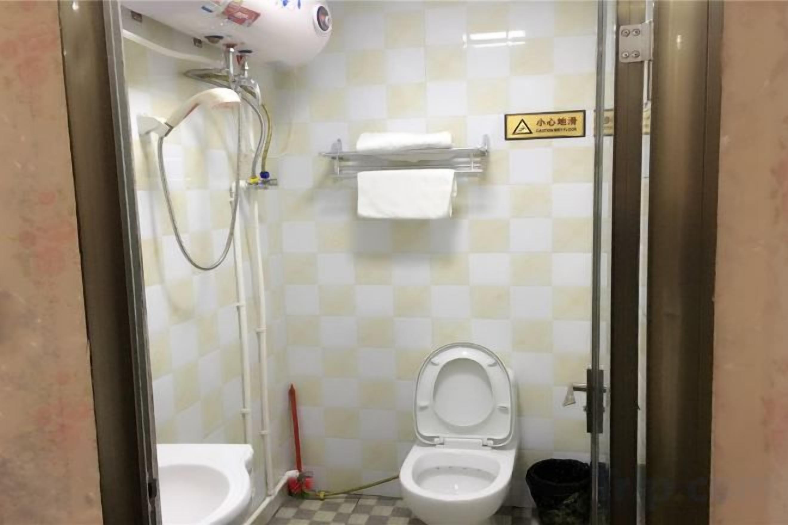 A bathroom with a shower, two toilets, and a towel rack.