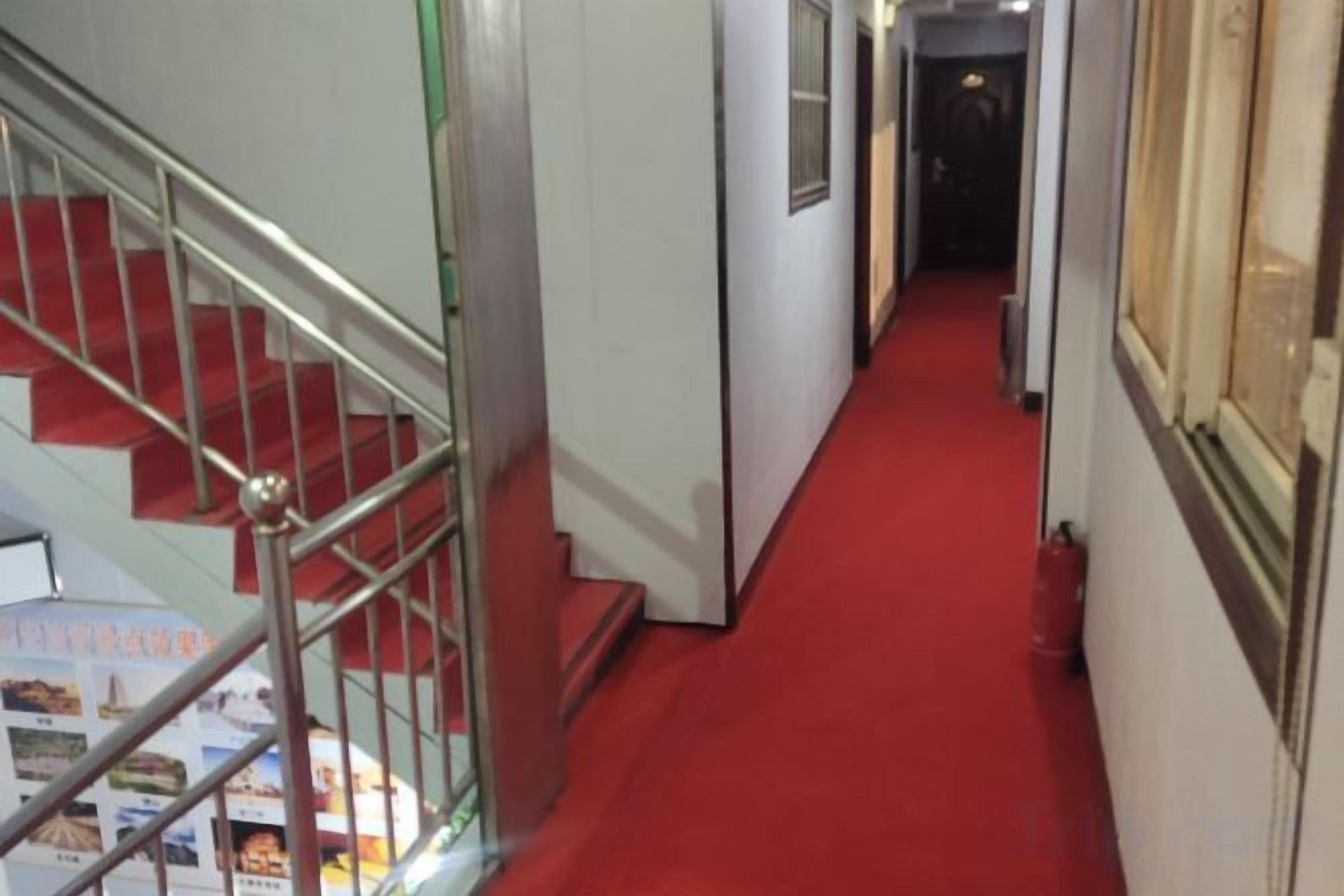 Un pasillo con alfombra roja que conduce a una escalera con barandillas de metal.
