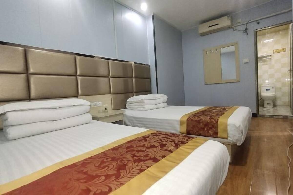 A hotel room with two beds, a headboard, a mirror, and a bathroom door.