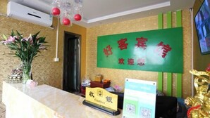 A hotel reception area with a green sign, a cash register, and a decorative plant. - Xi'an Lianhu District Hospitality Hotel (Xi'an)