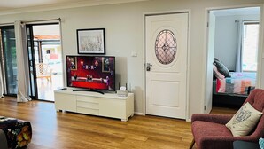 Een woonkamer met een televisie op een wit kastje, een deur met een decoratief glasraam en een rode fauteuil.