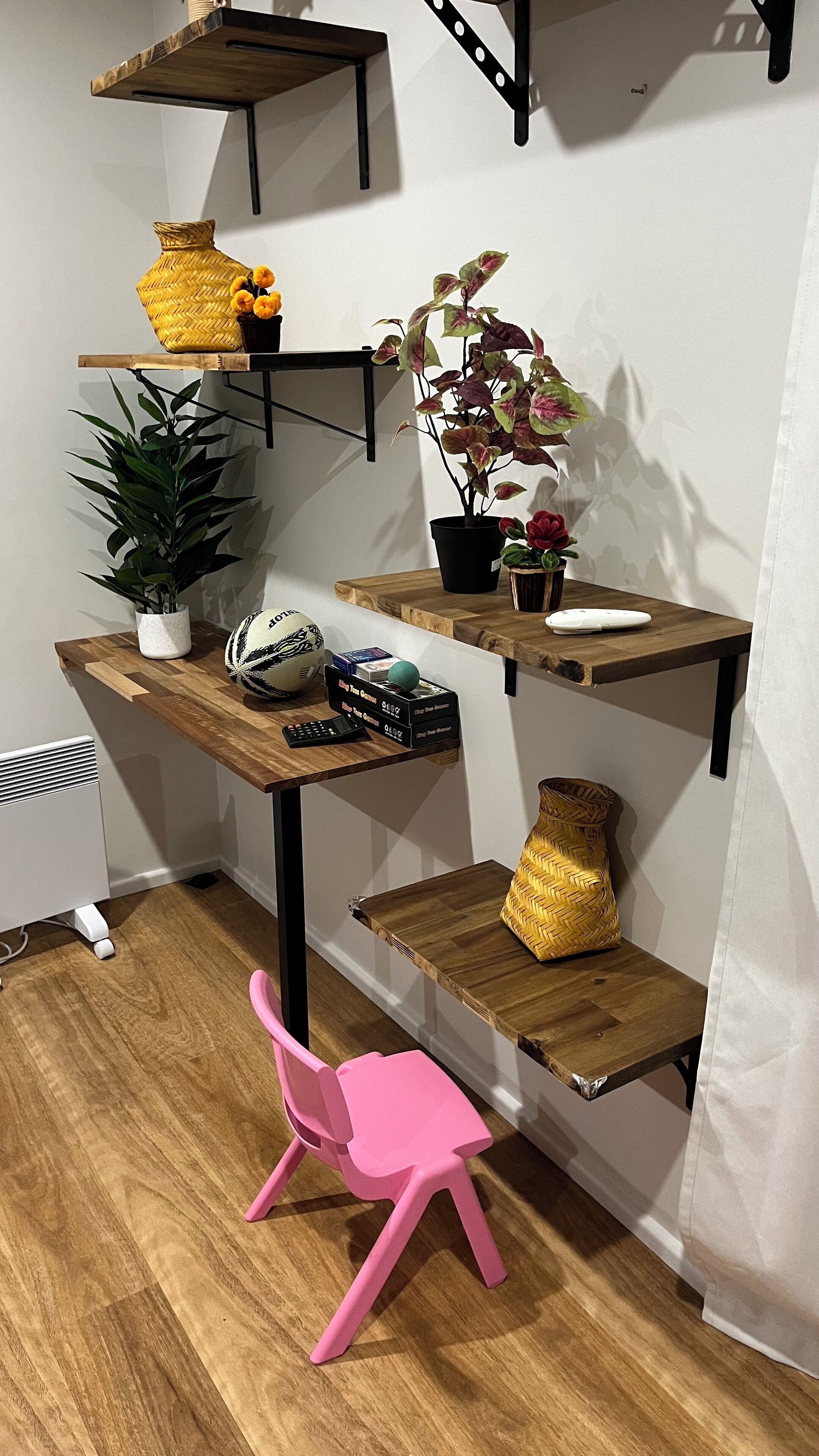 Ein kompakter Arbeitsbereich mit einem Holztisch, Regalen und einem rosa Stuhl.