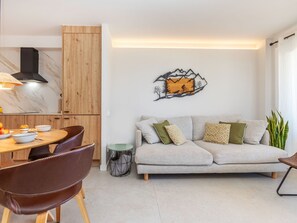A modern living room with a sofa, a dining table with chairs, a kitchen area, and a decorative wall piece.
