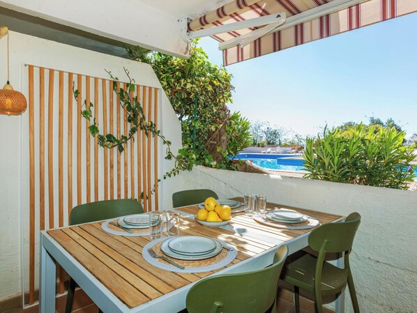An outdoor dining area with a wooden table, green chairs, and a view of a swimming pool.