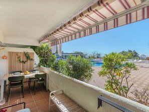 A balcony with a table and chairs, a view of a swimming pool, and a building in the background.