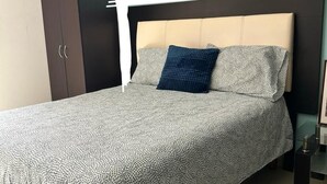 A bed with a patterned bedspread, a headboard, and a dark-colored wardrobe.