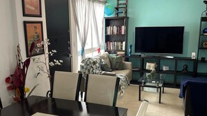 A living room with a dining table, chairs, a sofa, a TV, and a bookshelf.